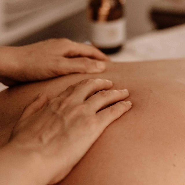 Masaje hidratante en la espalda con aceite, para un tratamiento corporal que aporta brillo (glow), en un ambiente de spa cálido.