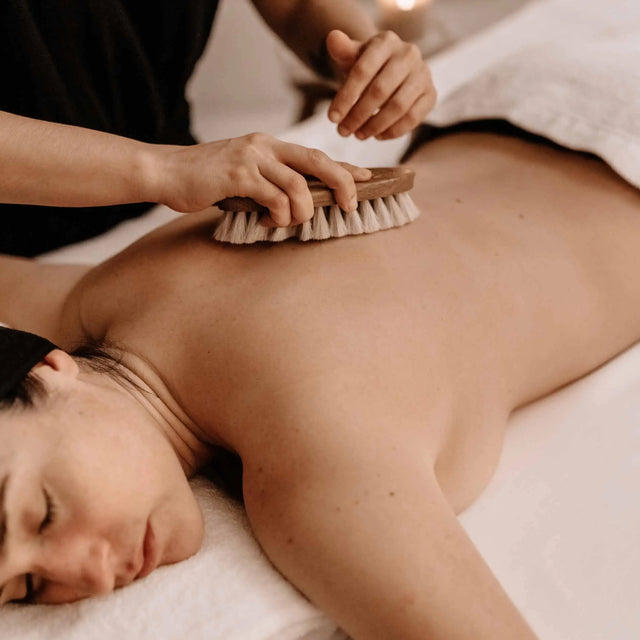 Tratamiento corporal relax con cepillado en seco en la espalda, utilizando un cepillo de madera para exfoliar y estimular la circulación.