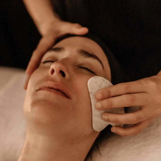 Masaje facial para glow o luminosidad con herramienta de piedra Guasha o Jade, enfocado en el drenaje y contorno del rostro, en un tratamiento de spa.
