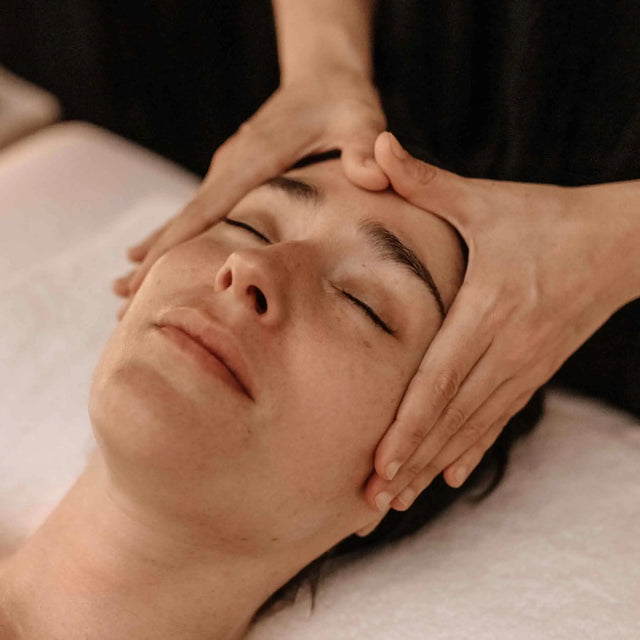 Primer plano de mujer joven recibiendo un masaje facial relajante o tratamiento de belleza en un spa. Manos aplicando presión en la frente para aliviar el estrés.