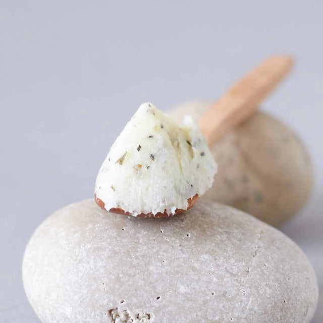 Muestra del Exfoliante y Masaje Posidonia (Scrub Massage) de textura blanca y cremosa con partículas, sobre una piedra de río, evocando ingredientes marinos.