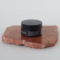 Envase de bálsamo facial desmaquillante de Beseaskin, 100% orgánico a base de manteca de mango y cacao, sobre piedra en una mesa blanca.