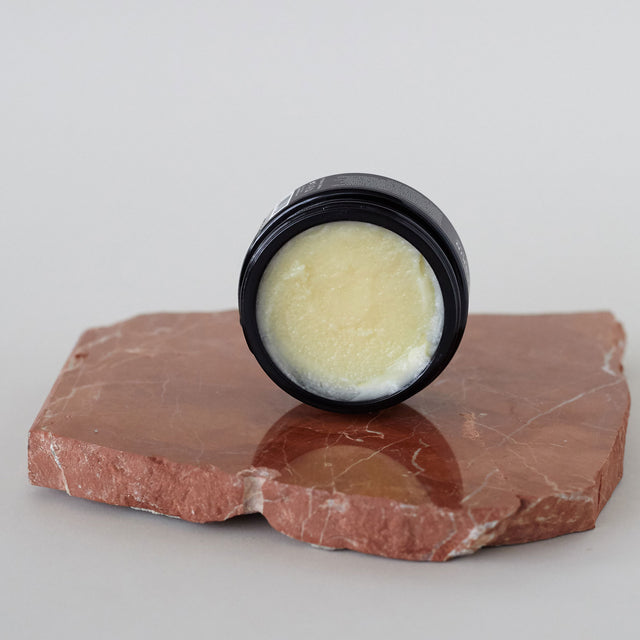 Envase de bálsamo facial desmaquillante de Beseaskin, 100% orgánico a base de manteca de mango y cacao, sobre piedra en una mesa blanca.