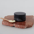 Envase de bálsamo facial desmaquillante de Beseaskin, 100% orgánico a base de manteca de mango y cacao, sobre piedra en una mesa blanca.