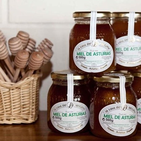 Frascos de Miel de de Asturias de 500g, 100% artesanal de La Casa del Apicultor, al lado de cesto con cucharas de miel