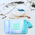 Neceser con estampado de lengua mallorquina con colores blancos, azules y turquesas y logo de SeaSkin Life en el centro, al lado de una cerámica de SeaSkin Life.