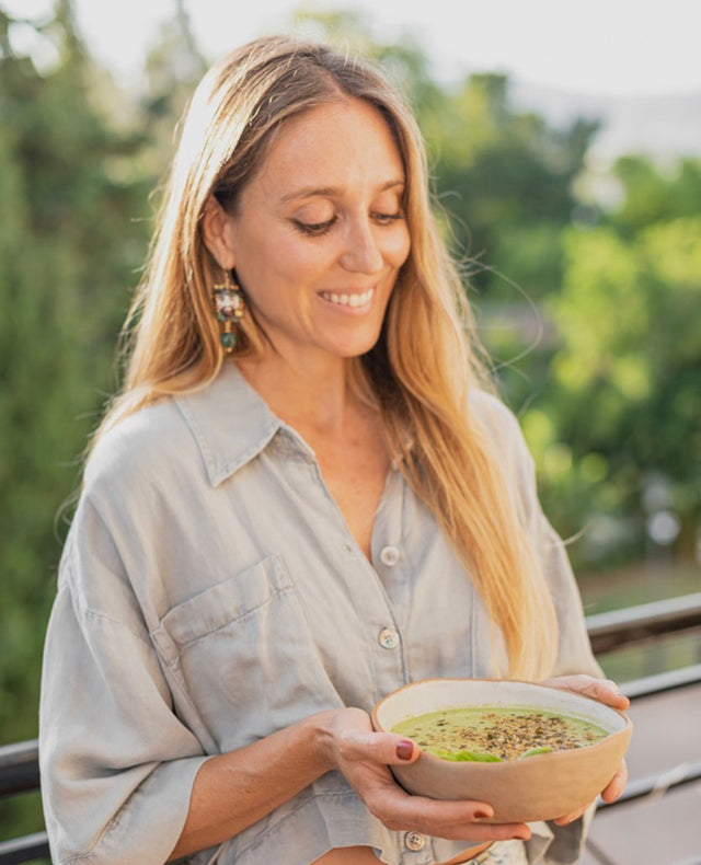Imagen de Paloma Ruiz, sonriente, con el pelo suelto, sujetando un cuenco con una crema de verduras en su interior.