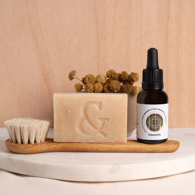 Envase de Elixir Intención (Skinbooster) junto a Jabon Orgánico Artesanal (regenerador) y Cepillo Facial de roble y pelo de cabra, 100% orgánicos sobre tabla de mármol